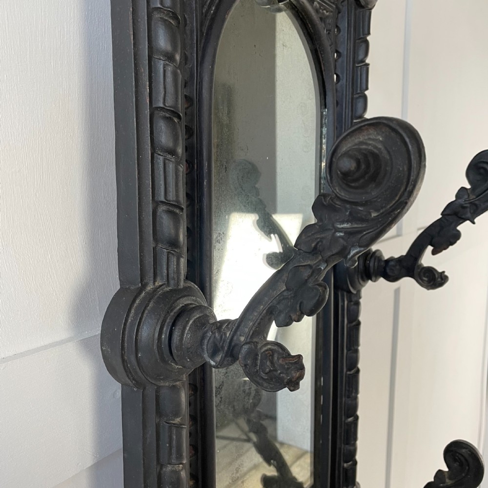 A tall black cast iron Victorian hall stand featuring an integrated central mirror, branching coat hooks, scrollwork tracery, and an umbrella drip tray at the base. View VI