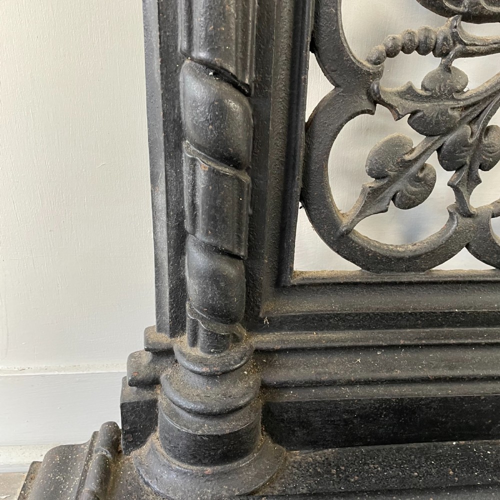 A tall black cast iron Victorian hall stand featuring an integrated central mirror, branching coat hooks, scrollwork tracery, and an umbrella drip tray at the base. View X