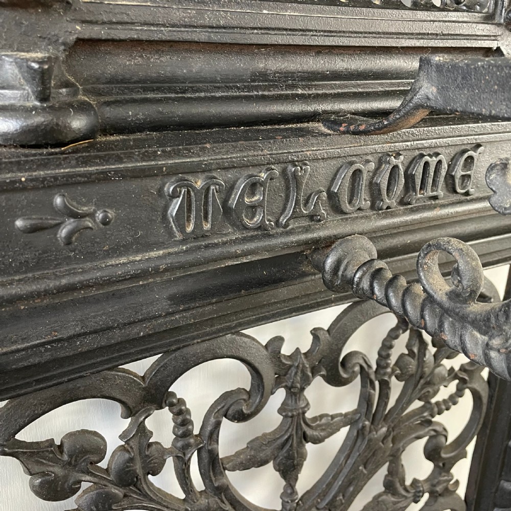 A tall black cast iron Victorian hall stand featuring an integrated central mirror, branching coat hooks, scrollwork tracery, and an umbrella drip tray at the base. View XI