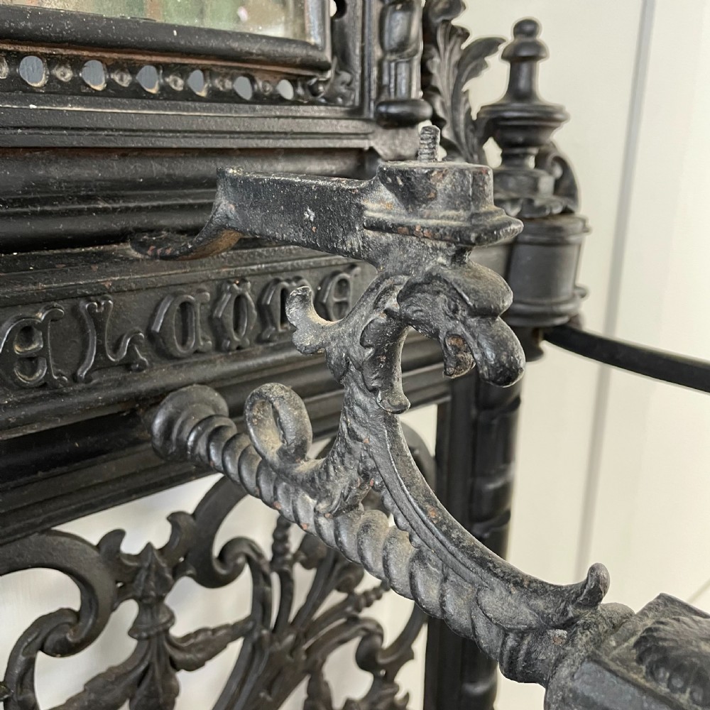 A tall black cast iron Victorian hall stand featuring an integrated central mirror, branching coat hooks, scrollwork tracery, and an umbrella drip tray at the base. View XVI