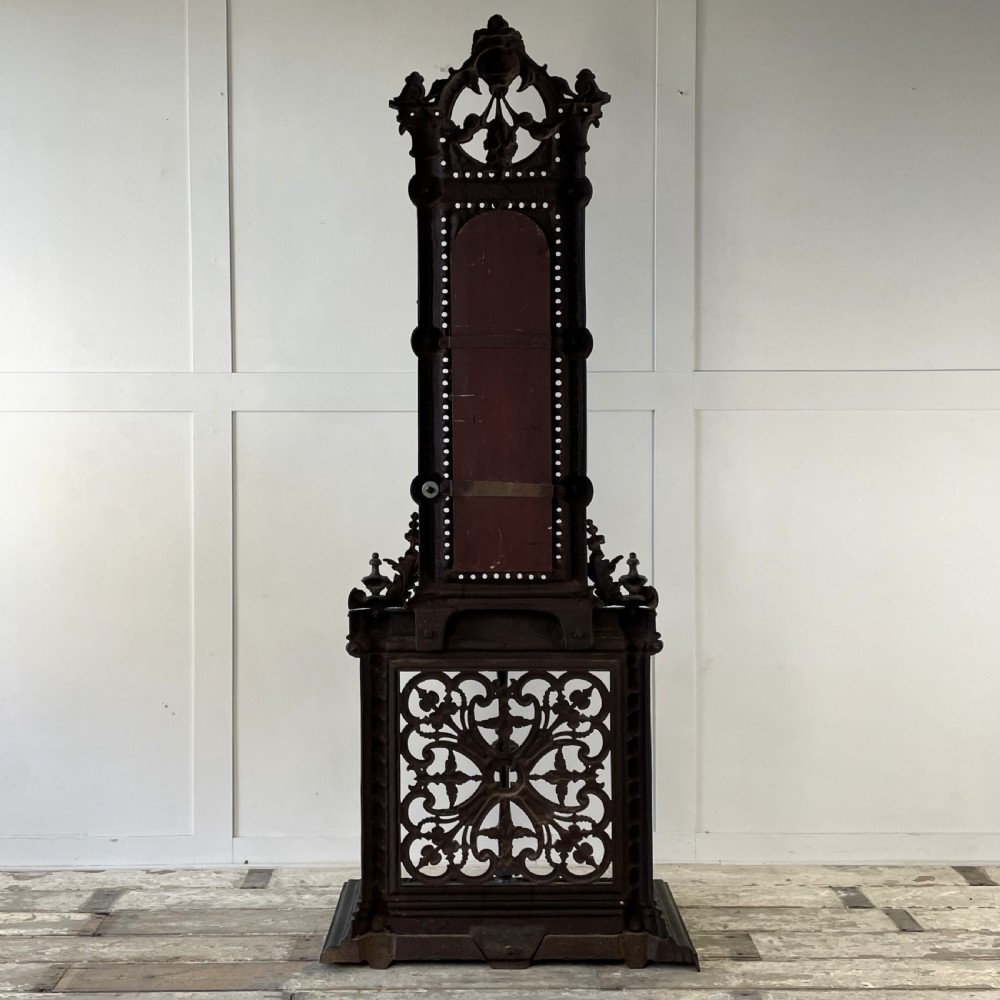 A tall black cast iron Victorian hall stand featuring an integrated central mirror, branching coat hooks, scrollwork tracery, and an umbrella drip tray at the base. View XVIII