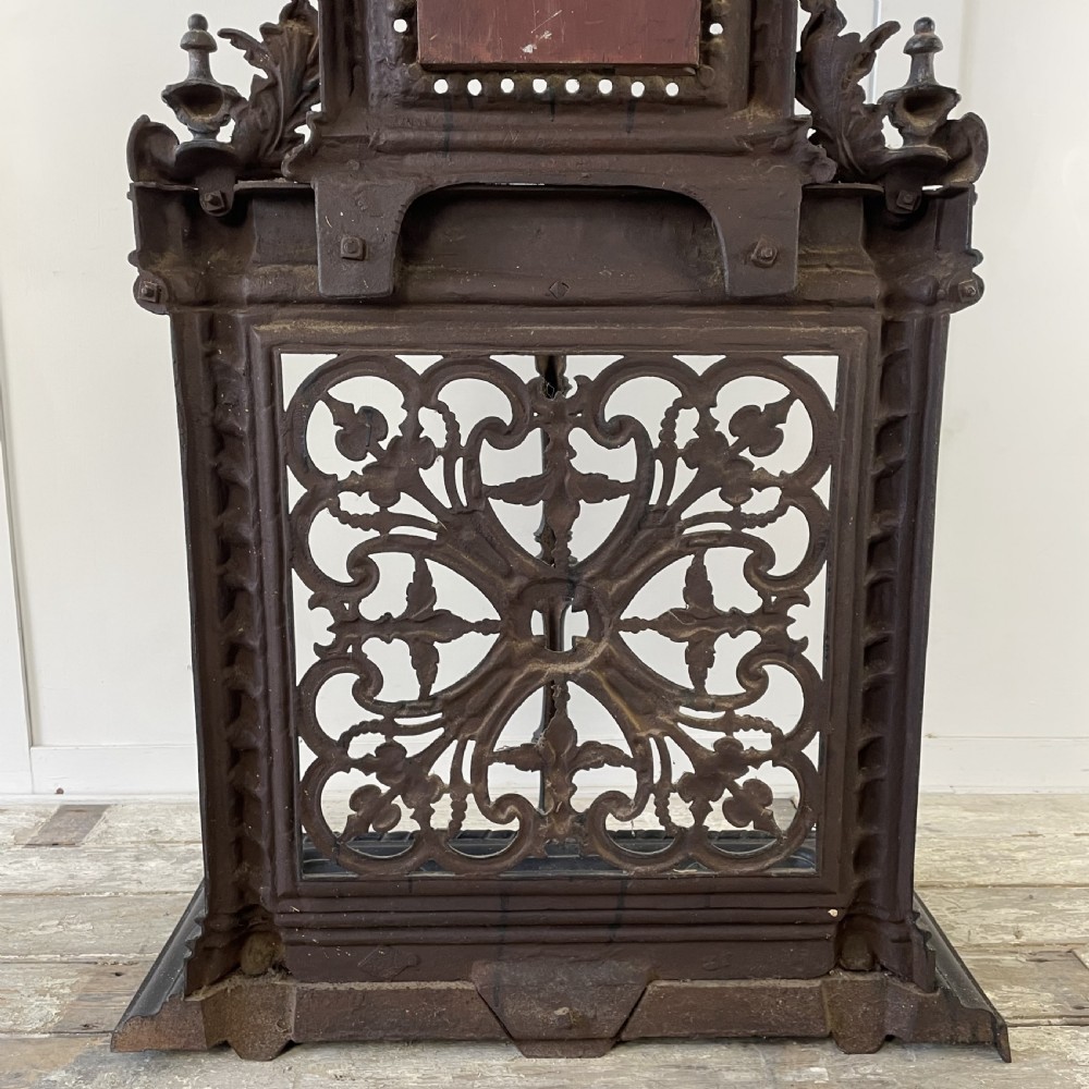 A tall black cast iron Victorian hall stand featuring an integrated central mirror, branching coat hooks, scrollwork tracery, and an umbrella drip tray at the base. View XXI