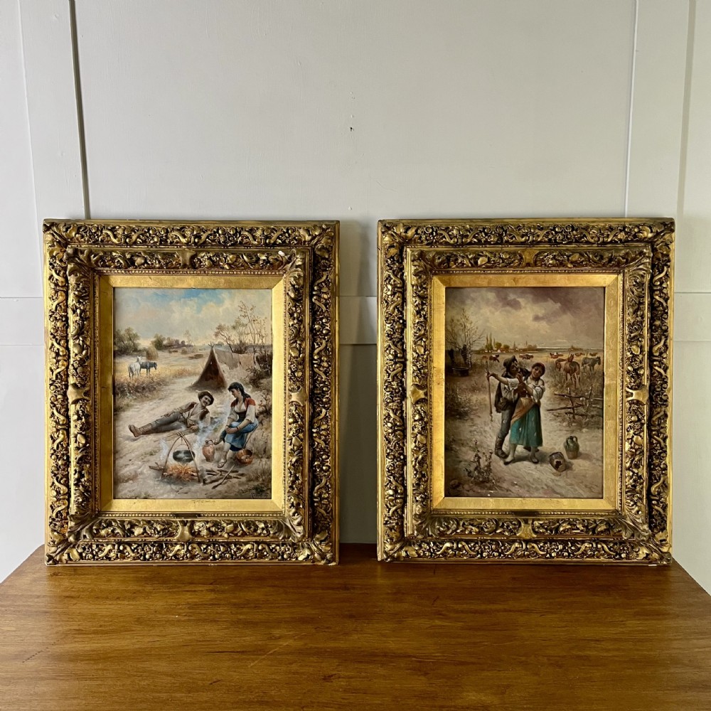 A pair of matching 19th-century oil paintings on board depicting rural peasant scenes in ornate carved gold gilt frames.