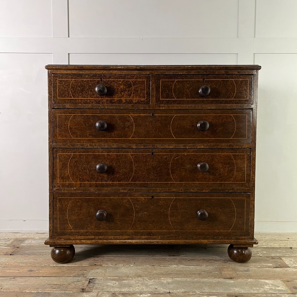 A nineteenth-century scumble-painted pine chest of drawers with decorative faux inlay lines, dark turned handles, and ball feet.