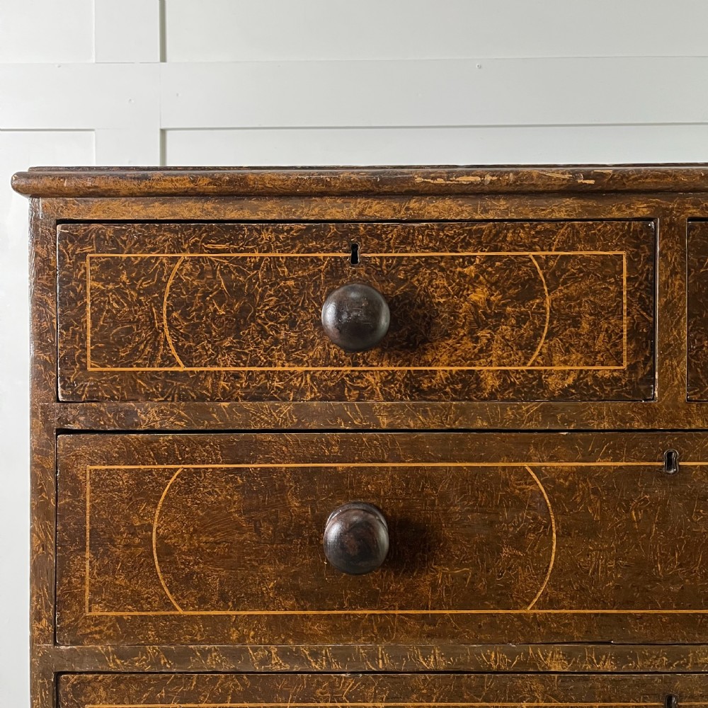 A nineteenth-century scumble-painted pine chest of drawers with decorative faux inlay lines, dark turned handles, and ball feet. View II