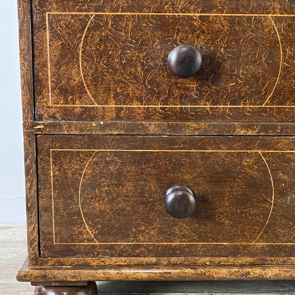 A nineteenth-century scumble-painted pine chest of drawers with decorative faux inlay lines, dark turned handles, and ball feet. View V