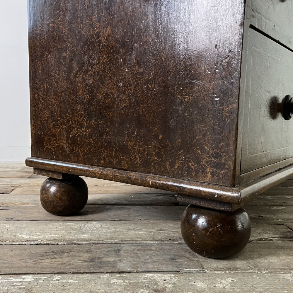 A nineteenth-century scumble-painted pine chest of drawers with decorative faux inlay lines, dark turned handles, and ball feet. View XXI