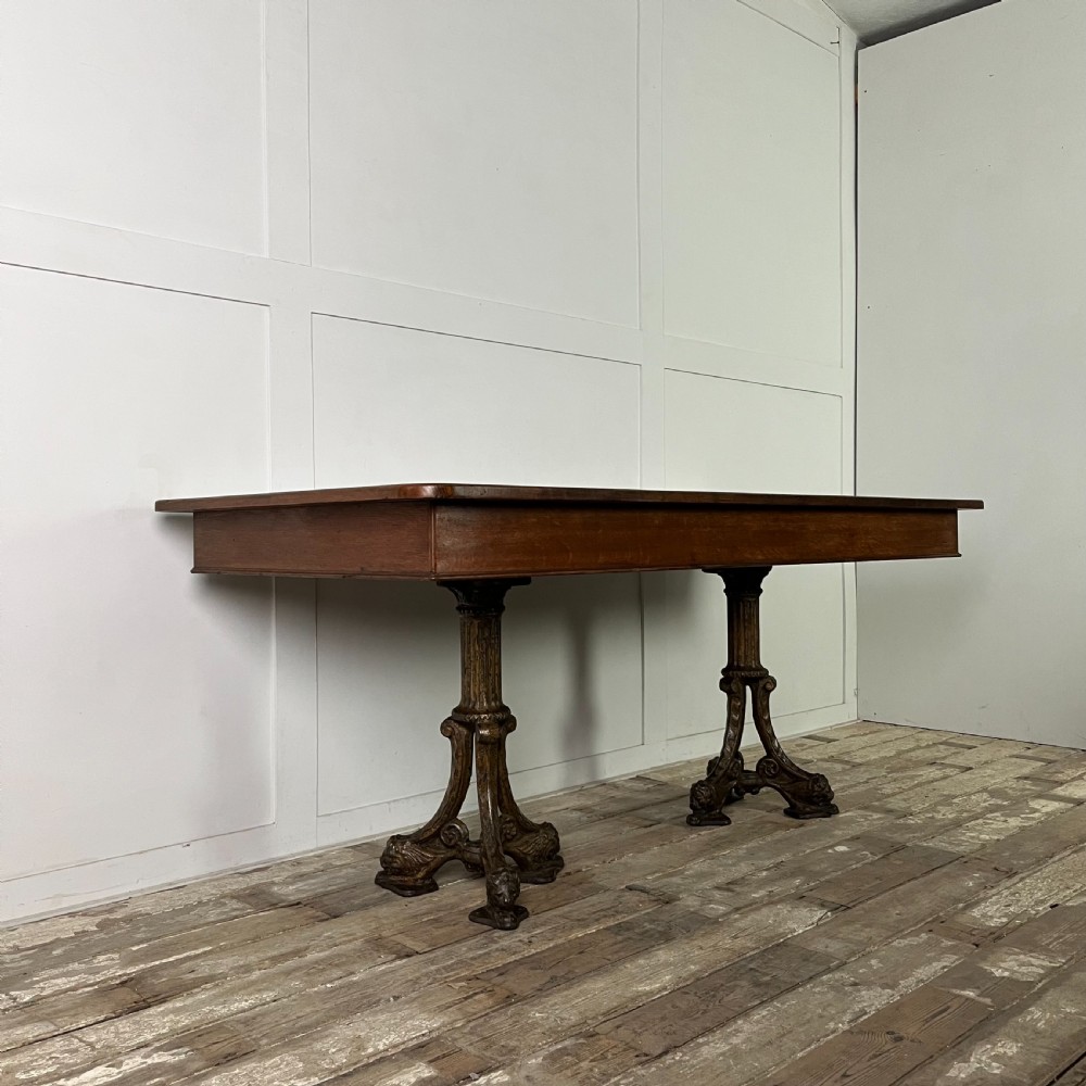 A long rectangular Victorian oak table featuring a thick wooden top resting on two ornate cast-iron pedestal legs. View VI