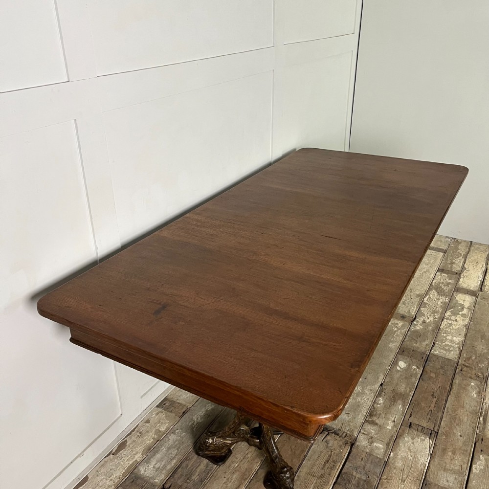 A long rectangular Victorian oak table featuring a thick wooden top resting on two ornate cast-iron pedestal legs. View VII