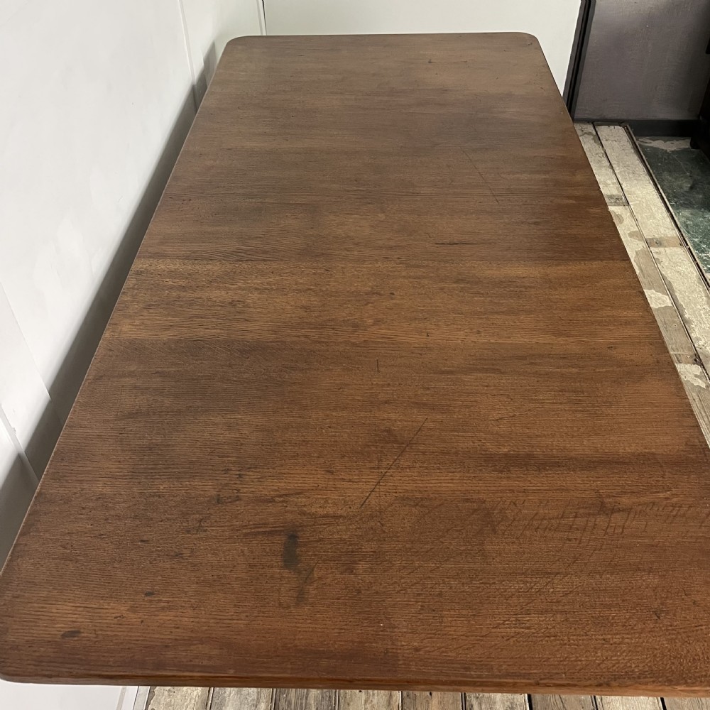 A long rectangular Victorian oak table featuring a thick wooden top resting on two ornate cast-iron pedestal legs. View VIII