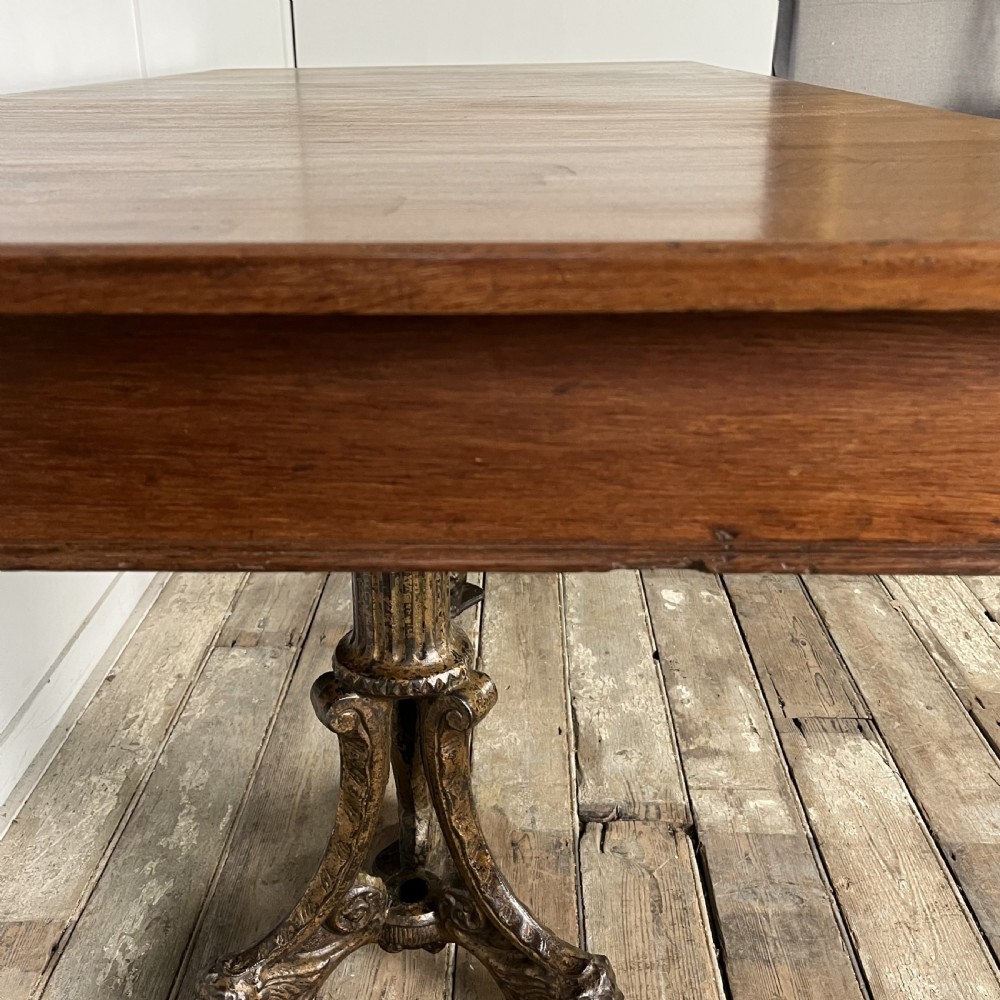 A long rectangular Victorian oak table featuring a thick wooden top resting on two ornate cast-iron pedestal legs. View IX