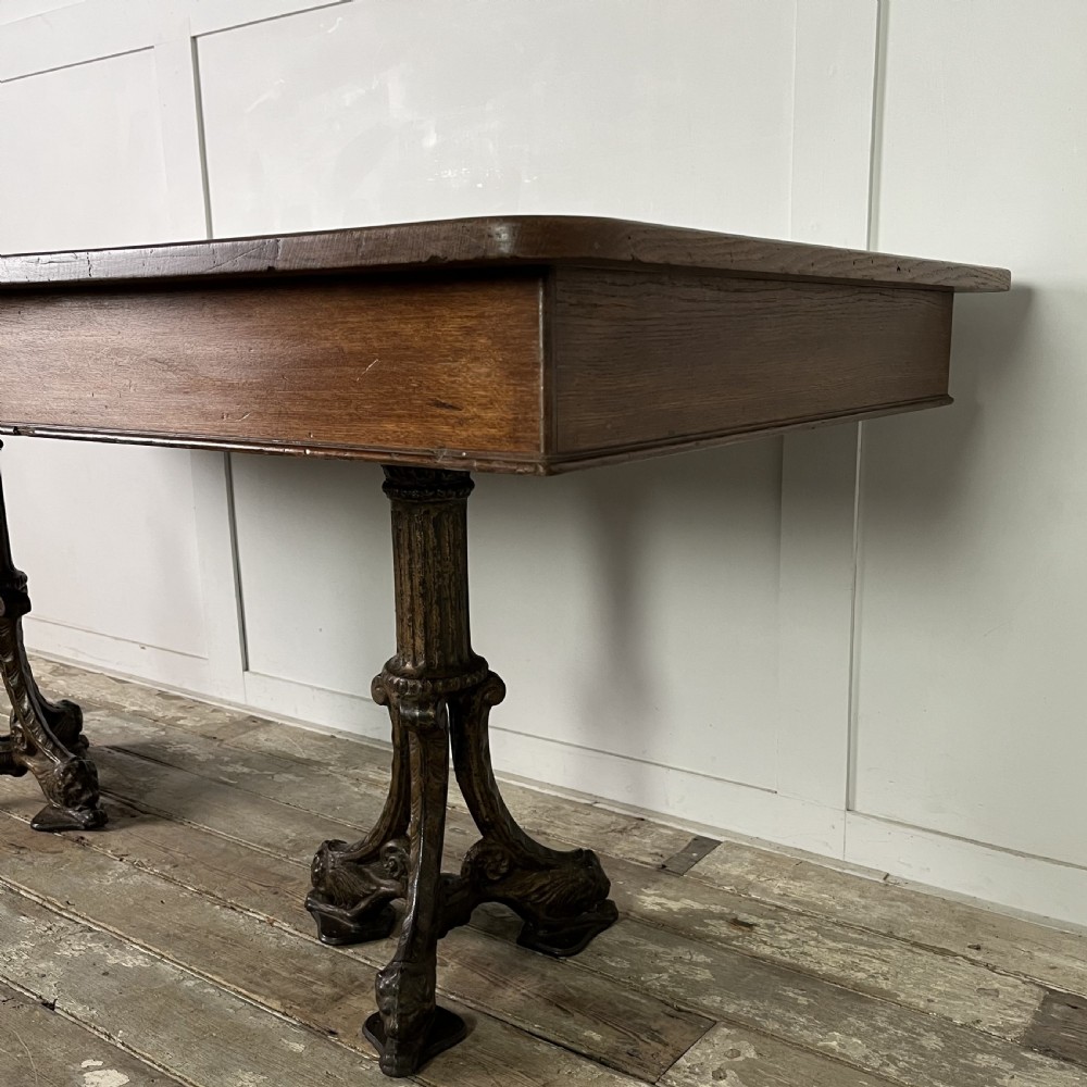 A long rectangular Victorian oak table featuring a thick wooden top resting on two ornate cast-iron pedestal legs. View X