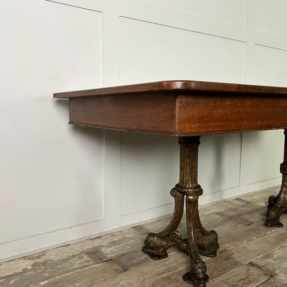 A long rectangular Victorian oak table featuring a thick wooden top resting on two ornate cast-iron pedestal legs. View XI