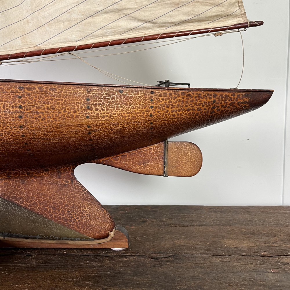 An Edwardian wooden pond yacht with a carved timber hull, tall rigged mast, cream fabric sails, and a wooden stand. View V
