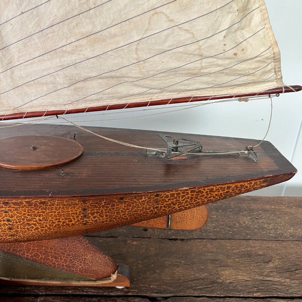 An Edwardian wooden pond yacht with a carved timber hull, tall rigged mast, cream fabric sails, and a wooden stand. View VI