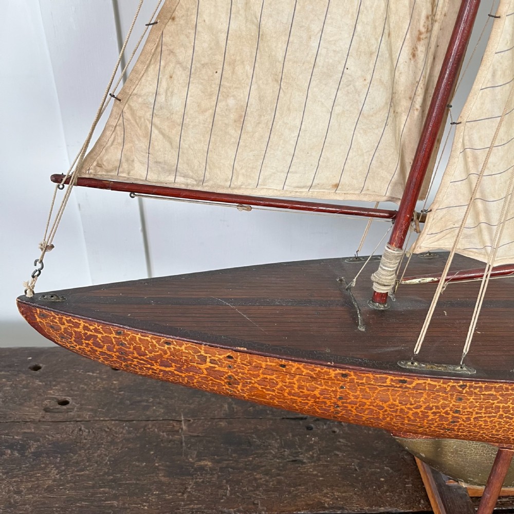 An Edwardian wooden pond yacht with a carved timber hull, tall rigged mast, cream fabric sails, and a wooden stand. View VII