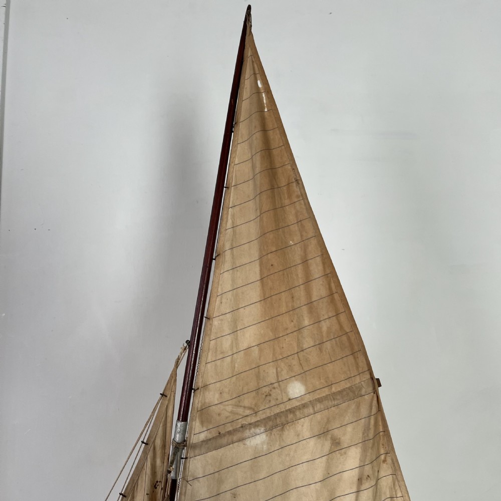 An Edwardian wooden pond yacht with a carved timber hull, tall rigged mast, cream fabric sails, and a wooden stand. View VIII