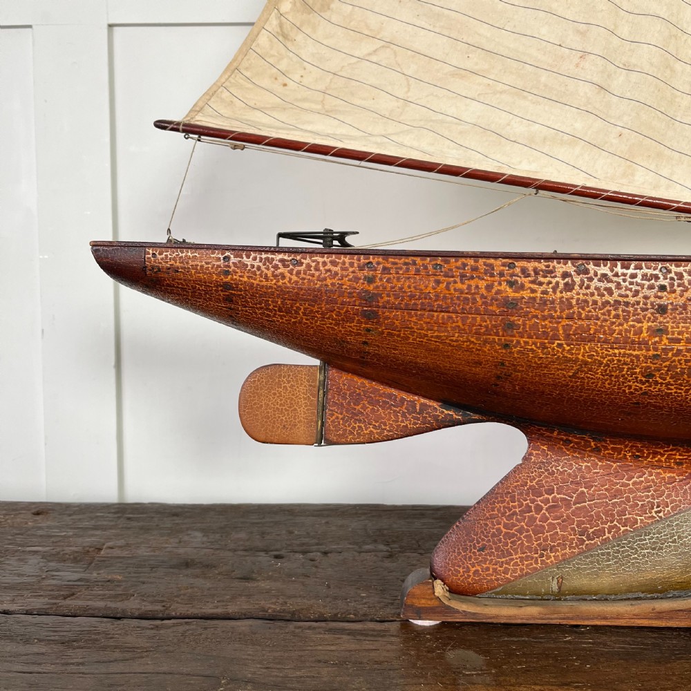 An Edwardian wooden pond yacht with a carved timber hull, tall rigged mast, cream fabric sails, and a wooden stand. View XI