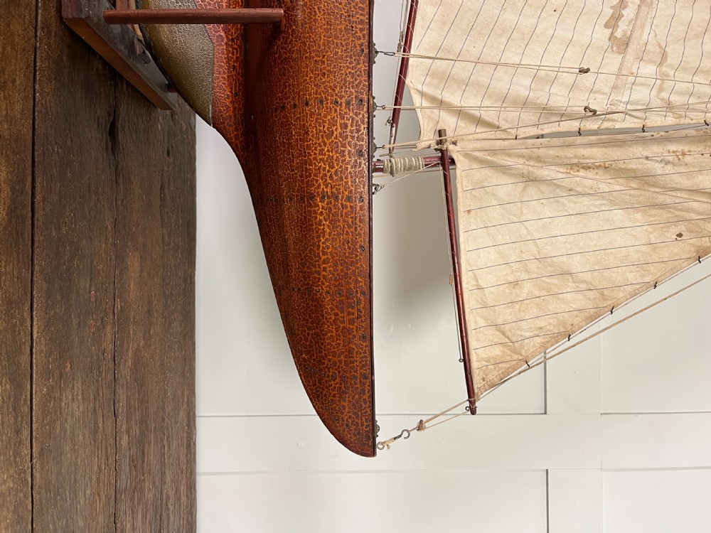 An Edwardian wooden pond yacht with a carved timber hull, tall rigged mast, cream fabric sails, and a wooden stand. View XII