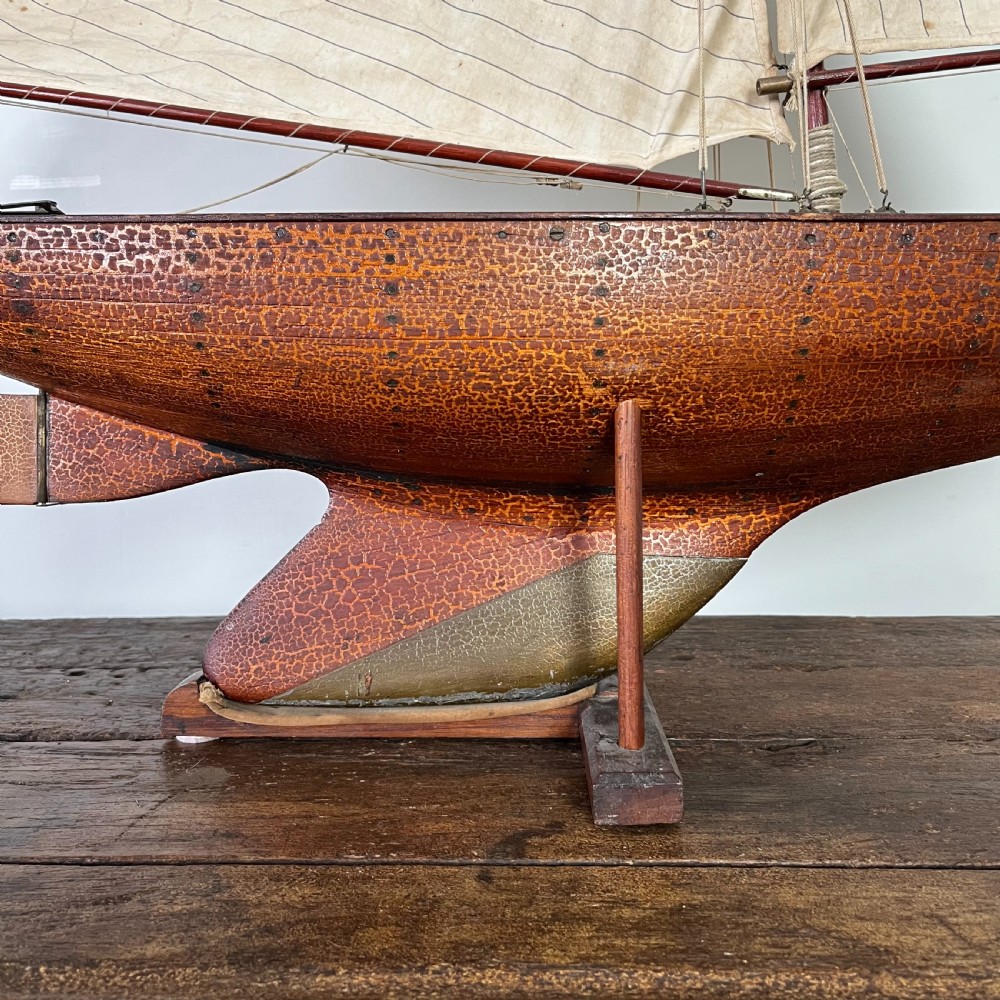An Edwardian wooden pond yacht with a carved timber hull, tall rigged mast, cream fabric sails, and a wooden stand. View XIII