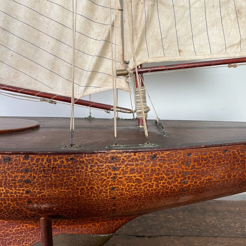 An Edwardian wooden pond yacht with a carved timber hull, tall rigged mast, cream fabric sails, and a wooden stand. View XIV