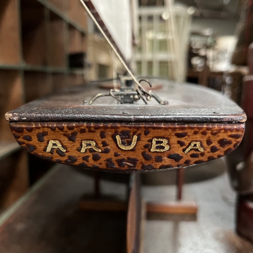 An Edwardian wooden pond yacht with a carved timber hull, tall rigged mast, cream fabric sails, and a wooden stand. View XVI