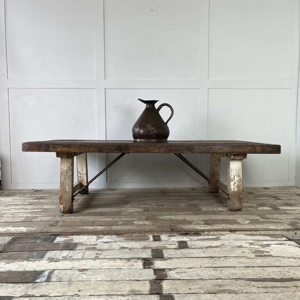 An early 20th-century rustic cheese press table featuring a thick dark wooden top and distressed painted trestle legs with metal bracing.