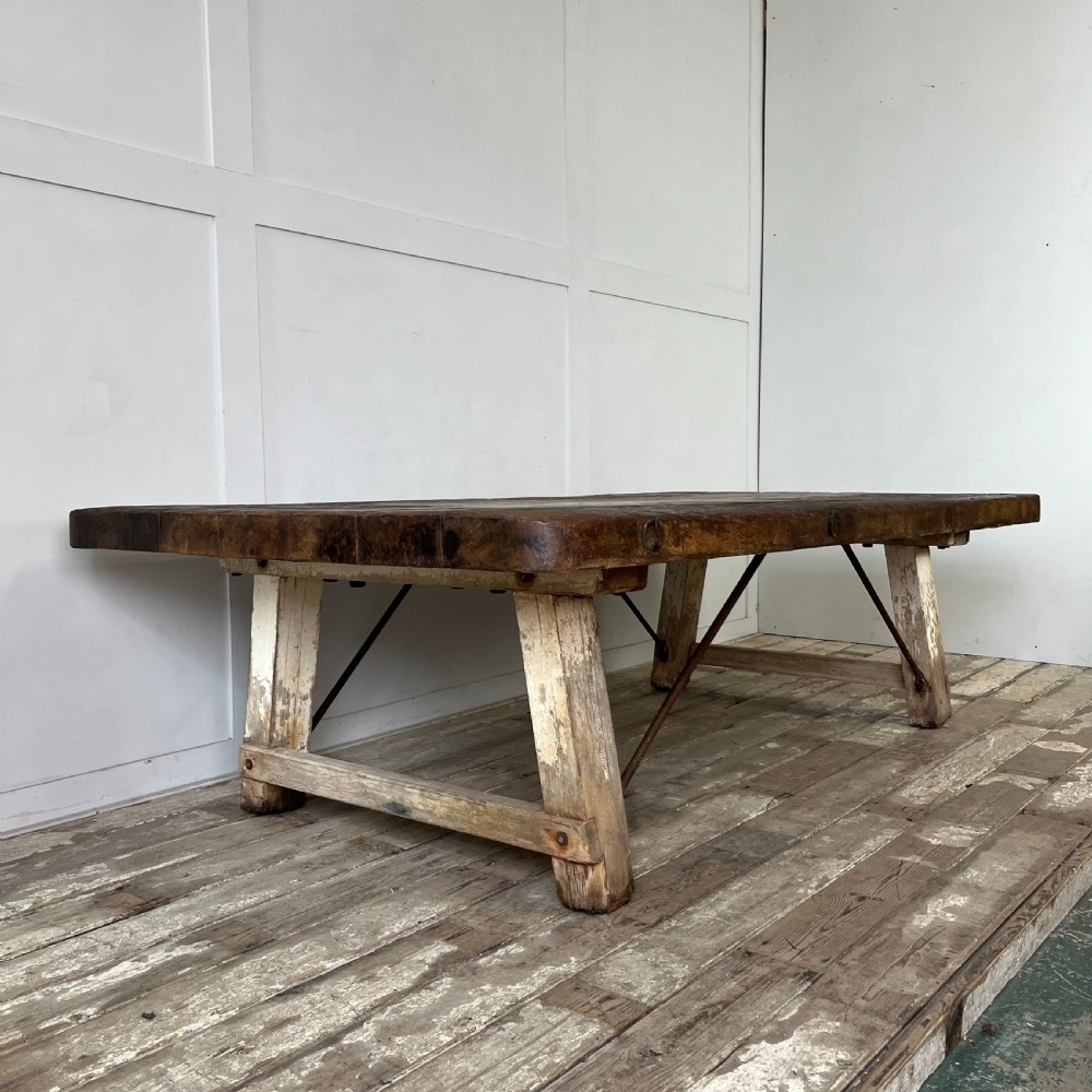 An early 20th-century rustic cheese press table featuring a thick dark wooden top and distressed painted trestle legs with metal bracing. View IV