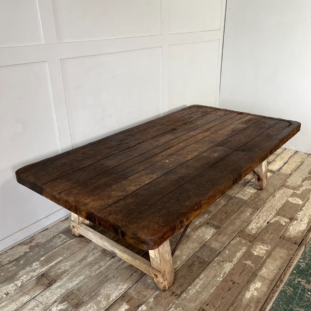 An early 20th-century rustic cheese press table featuring a thick dark wooden top and distressed painted trestle legs with metal bracing. View V