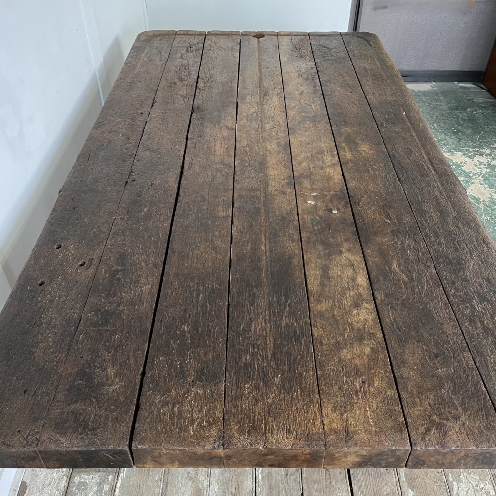An early 20th-century rustic cheese press table featuring a thick dark wooden top and distressed painted trestle legs with metal bracing. View VI