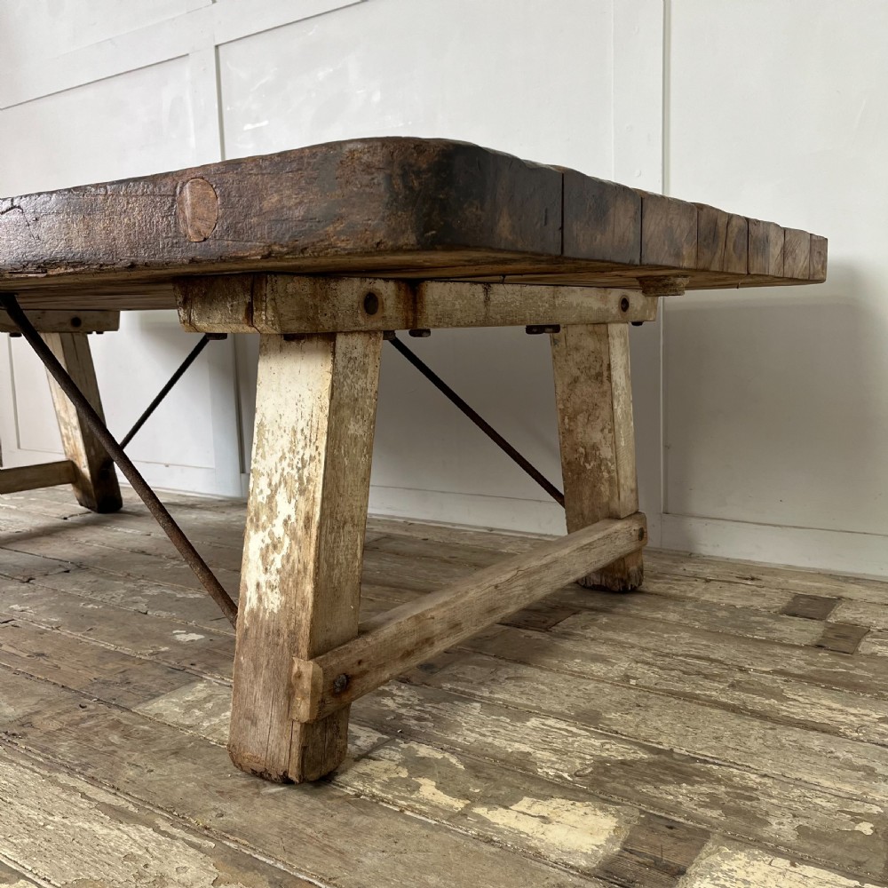 An early 20th-century rustic cheese press table featuring a thick dark wooden top and distressed painted trestle legs with metal bracing. View IX