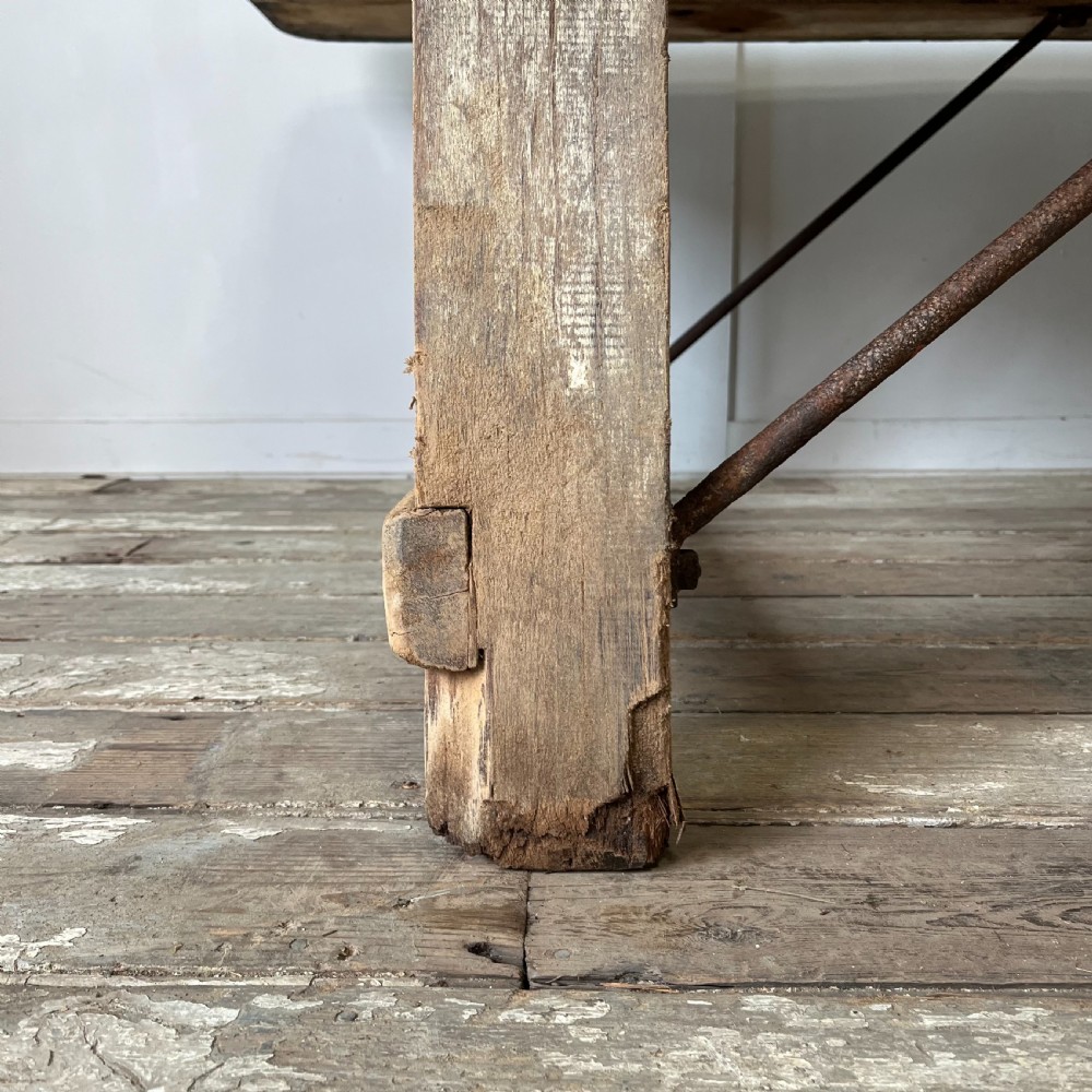 An early 20th-century rustic cheese press table featuring a thick dark wooden top and distressed painted trestle legs with metal bracing. View XI