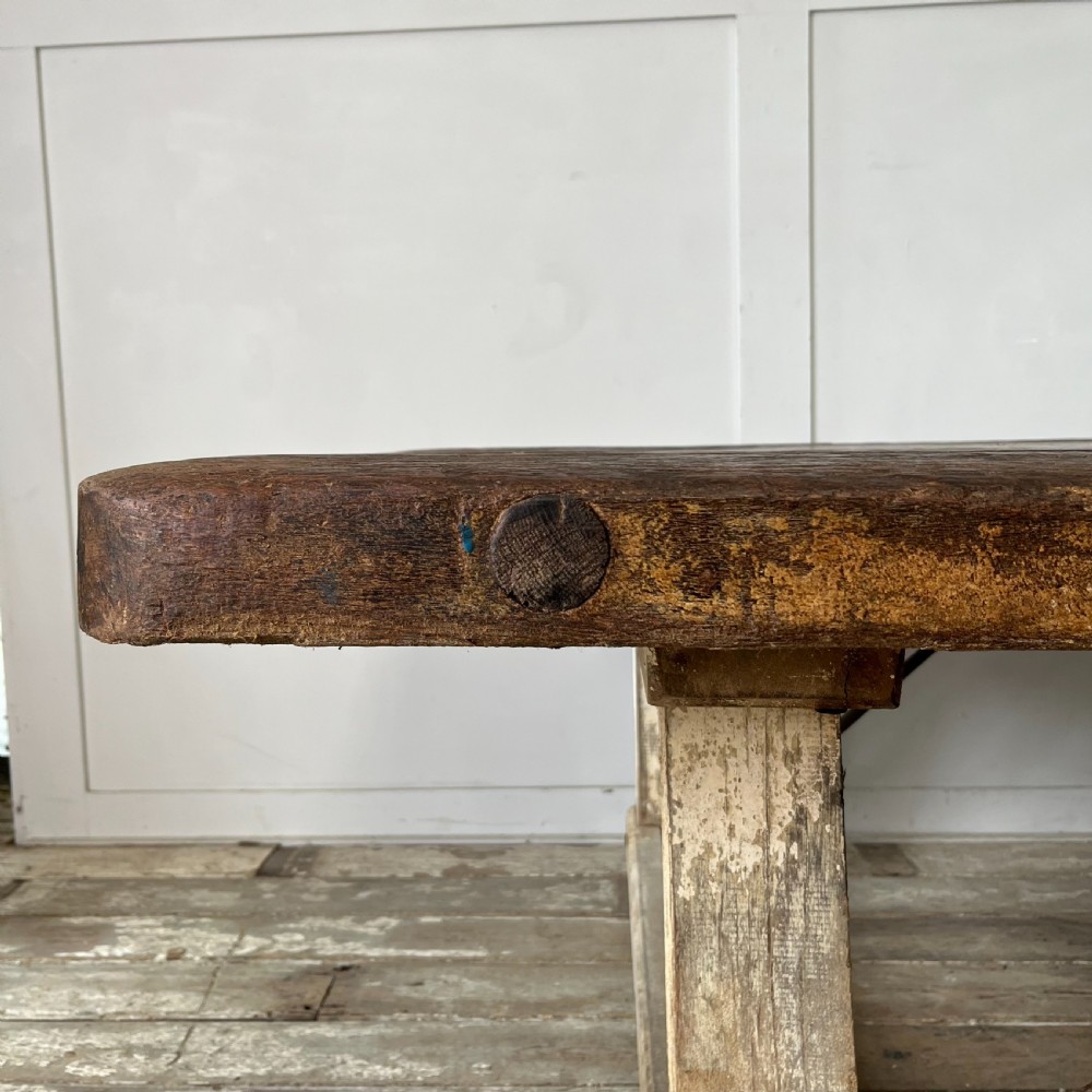 An early 20th-century rustic cheese press table featuring a thick dark wooden top and distressed painted trestle legs with metal bracing. View XII