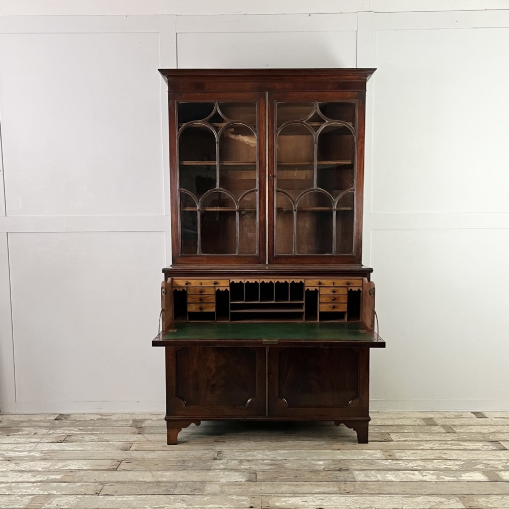 A dark mahogany George III secretaire bookcase featuring upper astragal glazed doors, a fold-out secretaire desk section with green leather insert, and lower cupboard doors on bracket feet.