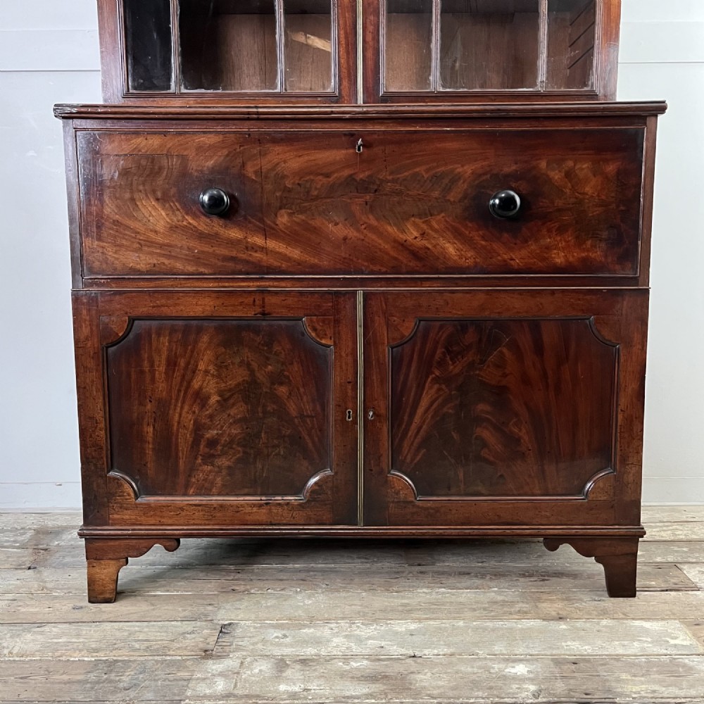 A dark mahogany George III secretaire bookcase featuring upper astragal glazed doors, a fold-out secretaire desk section with green leather insert, and lower cupboard doors on bracket feet. View VI