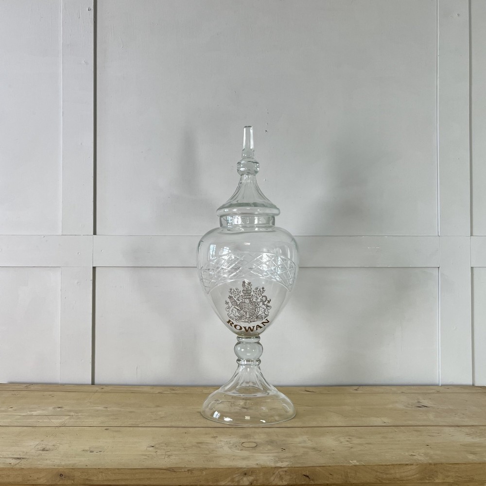 A clear cut glass Edwardian apothecary jar with a pointed finial lid, lattice shoulder pattern, and printed crest above the text ROWAN.