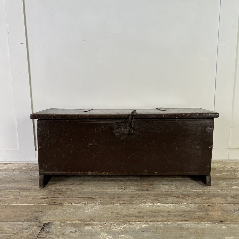 A dark brown 18th-century oak coffer with a flat hinged lid, iron hardware, and slab end supports.