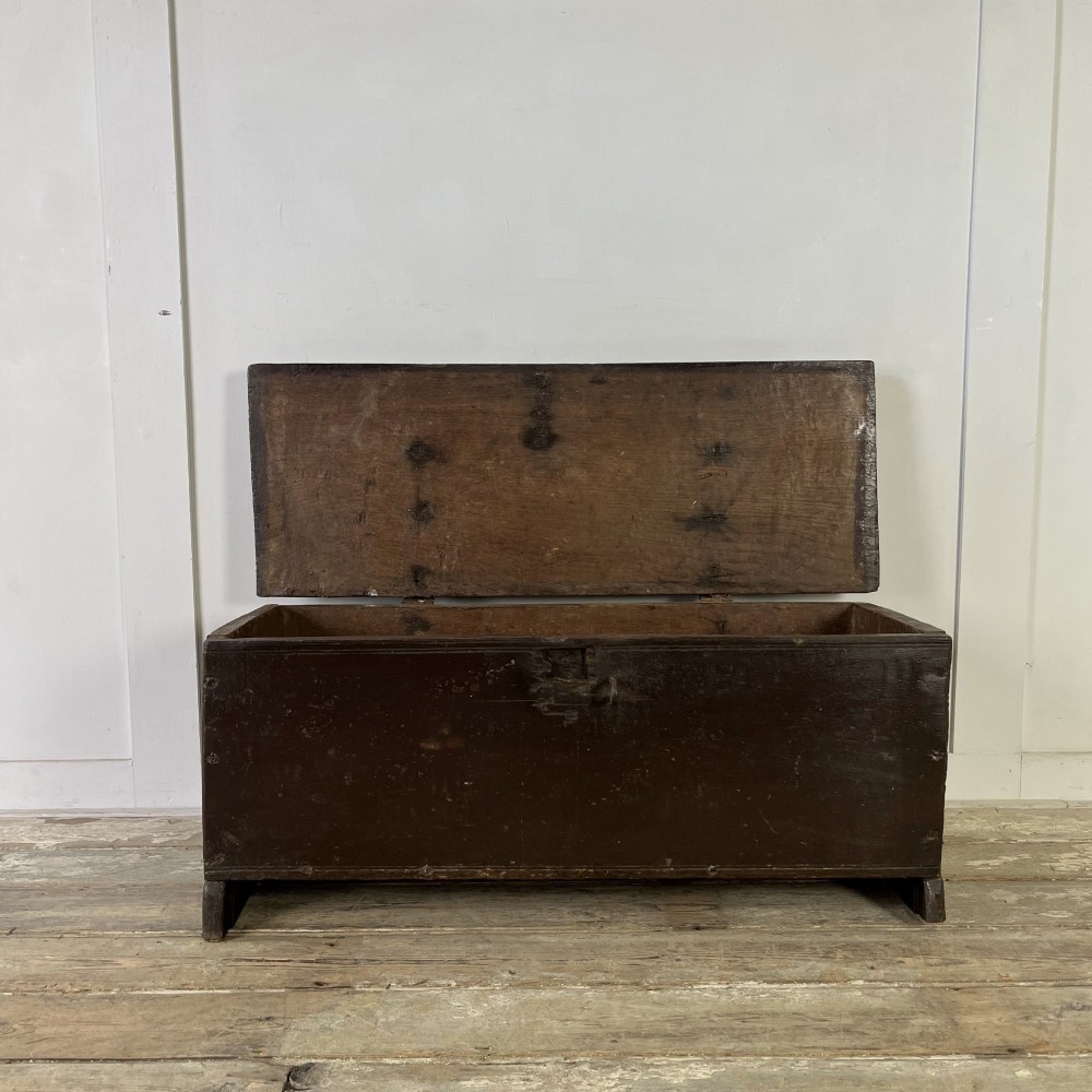 A dark brown 18th-century oak coffer with a flat hinged lid, iron hardware, and slab end supports. View II