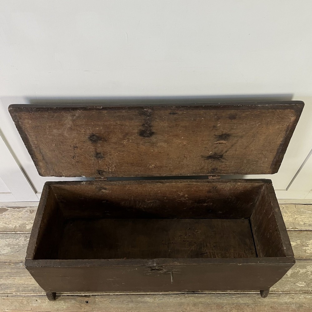 A dark brown 18th-century oak coffer with a flat hinged lid, iron hardware, and slab end supports. View V