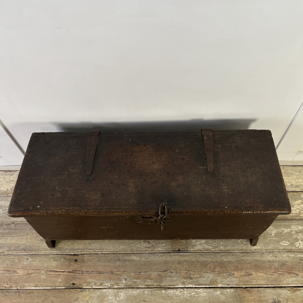 A dark brown 18th-century oak coffer with a flat hinged lid, iron hardware, and slab end supports. View VI