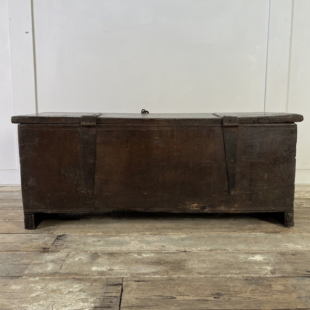 A dark brown 18th-century oak coffer with a flat hinged lid, iron hardware, and slab end supports. View X