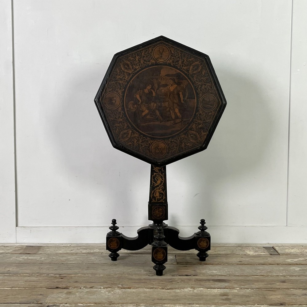 An early nineteenth-century octagonal ebonised tilt-top table featuring intricate ink-drawn classical figures and floral penwork borders.