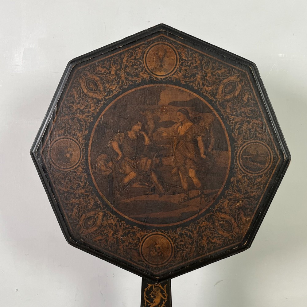 An early nineteenth-century octagonal ebonised tilt-top table featuring intricate ink-drawn classical figures and floral penwork borders. View II