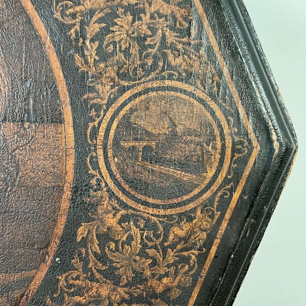An early nineteenth-century octagonal ebonised tilt-top table featuring intricate ink-drawn classical figures and floral penwork borders. View V