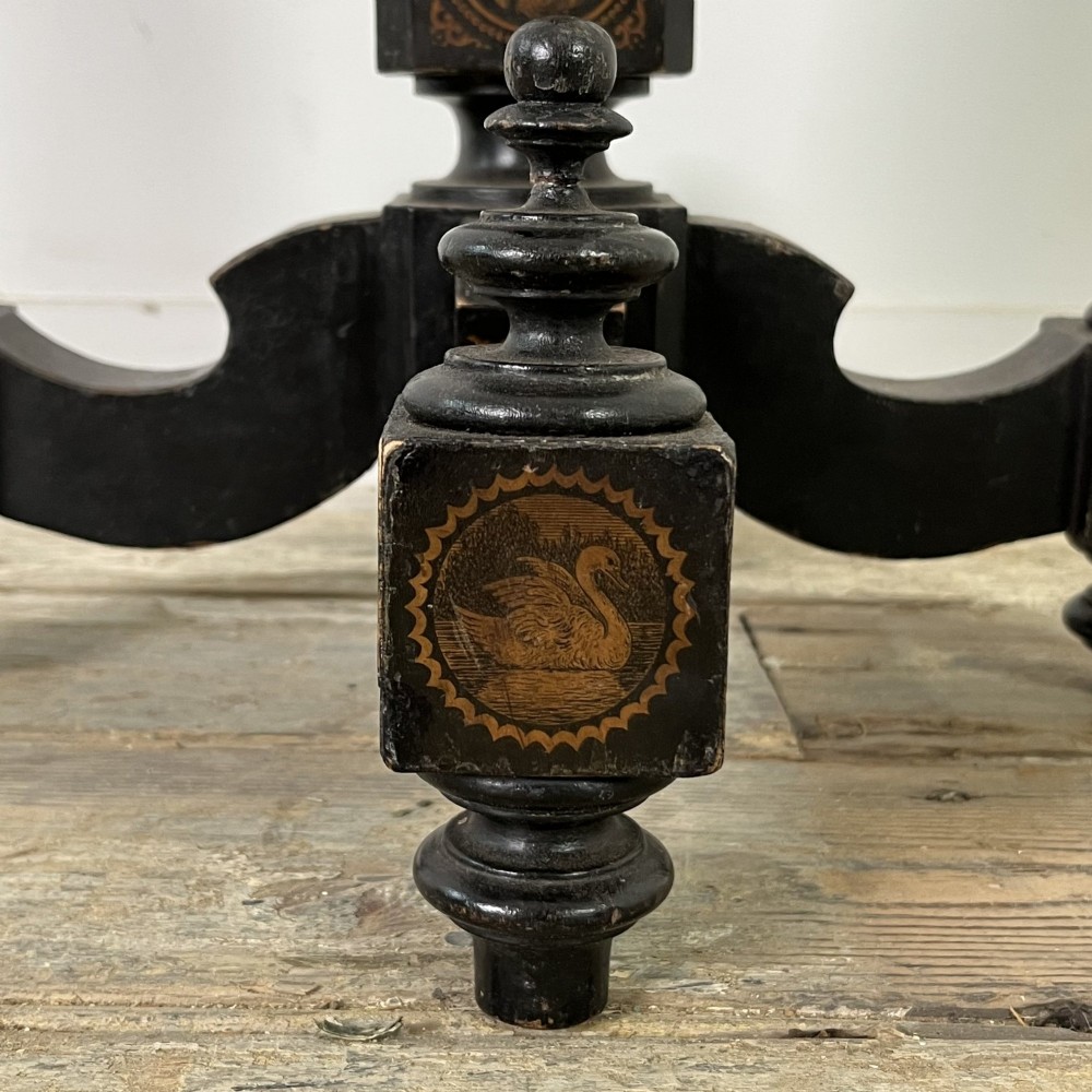 An early nineteenth-century octagonal ebonised tilt-top table featuring intricate ink-drawn classical figures and floral penwork borders. View VI