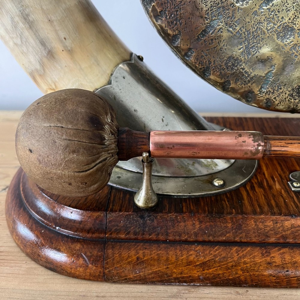 A Victorian tabletop dinner gong featuring two curved natural horns mounted on a polished oak base, holding a central hammered brass disc with an accompanying wooden striker. View VI