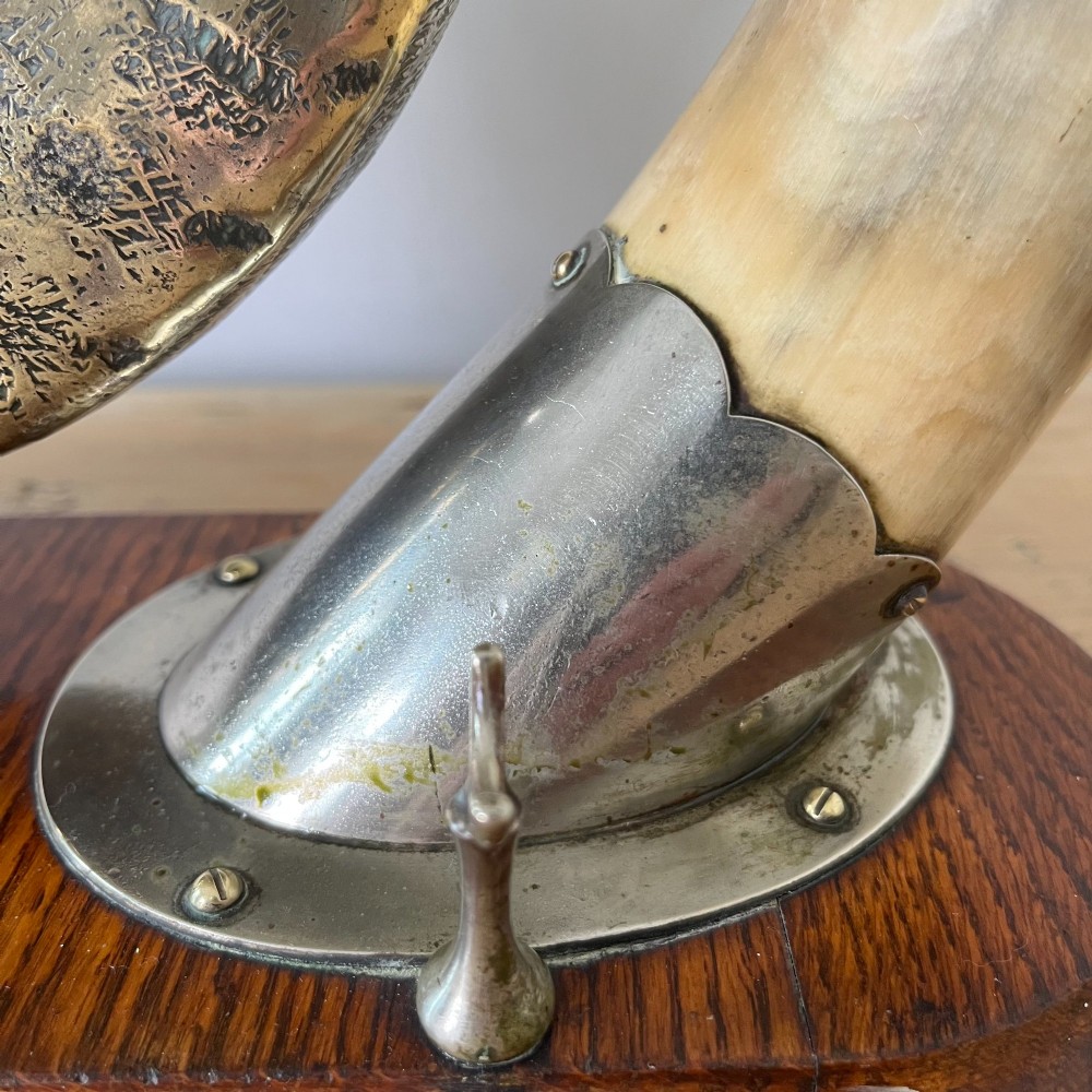 A Victorian tabletop dinner gong featuring two curved natural horns mounted on a polished oak base, holding a central hammered brass disc with an accompanying wooden striker. View VIII