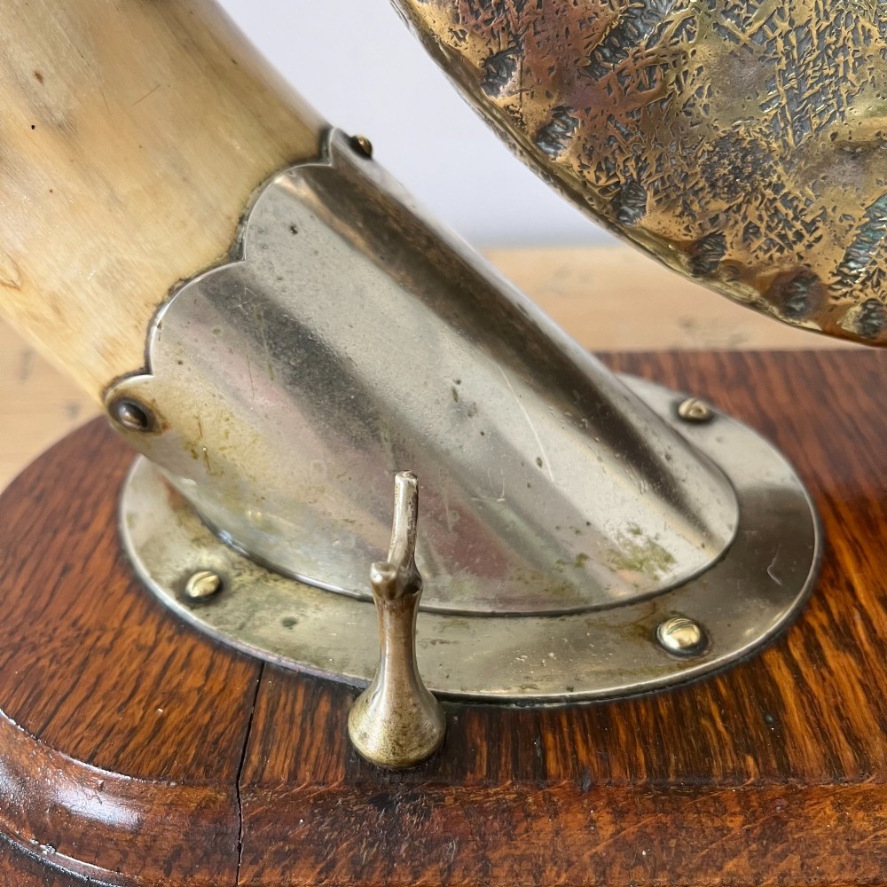 A Victorian tabletop dinner gong featuring two curved natural horns mounted on a polished oak base, holding a central hammered brass disc with an accompanying wooden striker. View IX