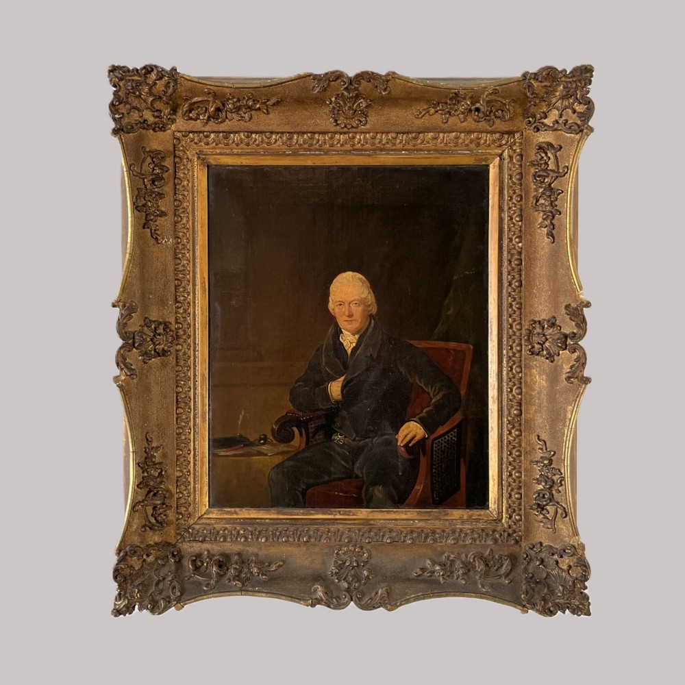 A 19th-century oil portrait depicting a seated gentleman in dark attire against a dark background, set within a heavily carved giltwood frame.