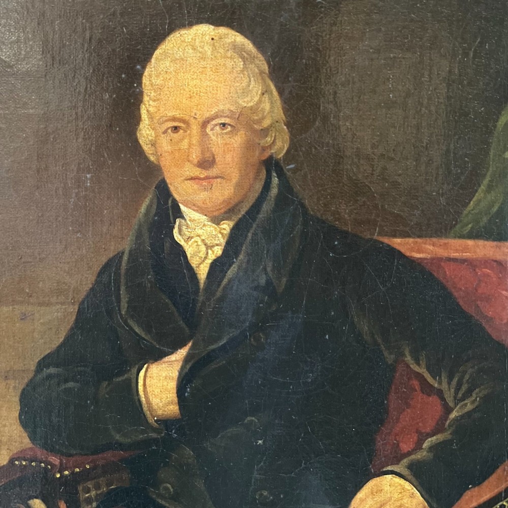 A 19th-century oil portrait depicting a seated gentleman in dark attire against a dark background, set within a heavily carved giltwood frame. View IV